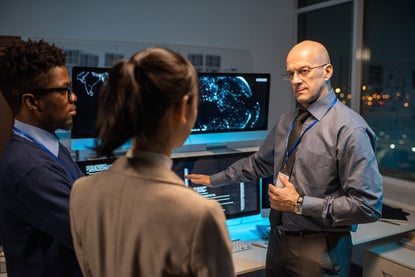 Director of software company giving instructions to team while pointing at data on computer screen