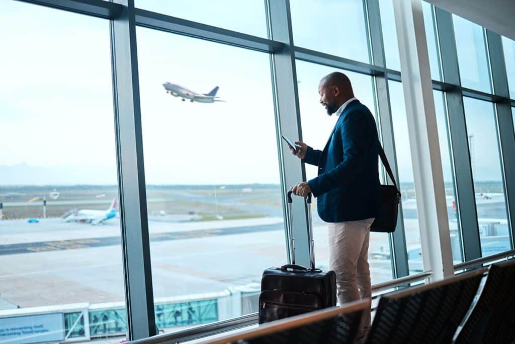 Business man with phone, airport window and plane taking off, checking flight schedule terminal for business trip. Technology, travel and businessman reading international travel restrictions app online.